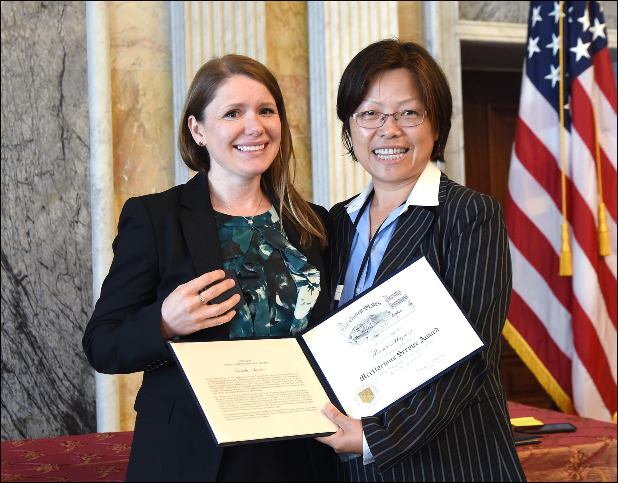 Two women smiling, standing side by side. Woman on the right is holding a certificate.